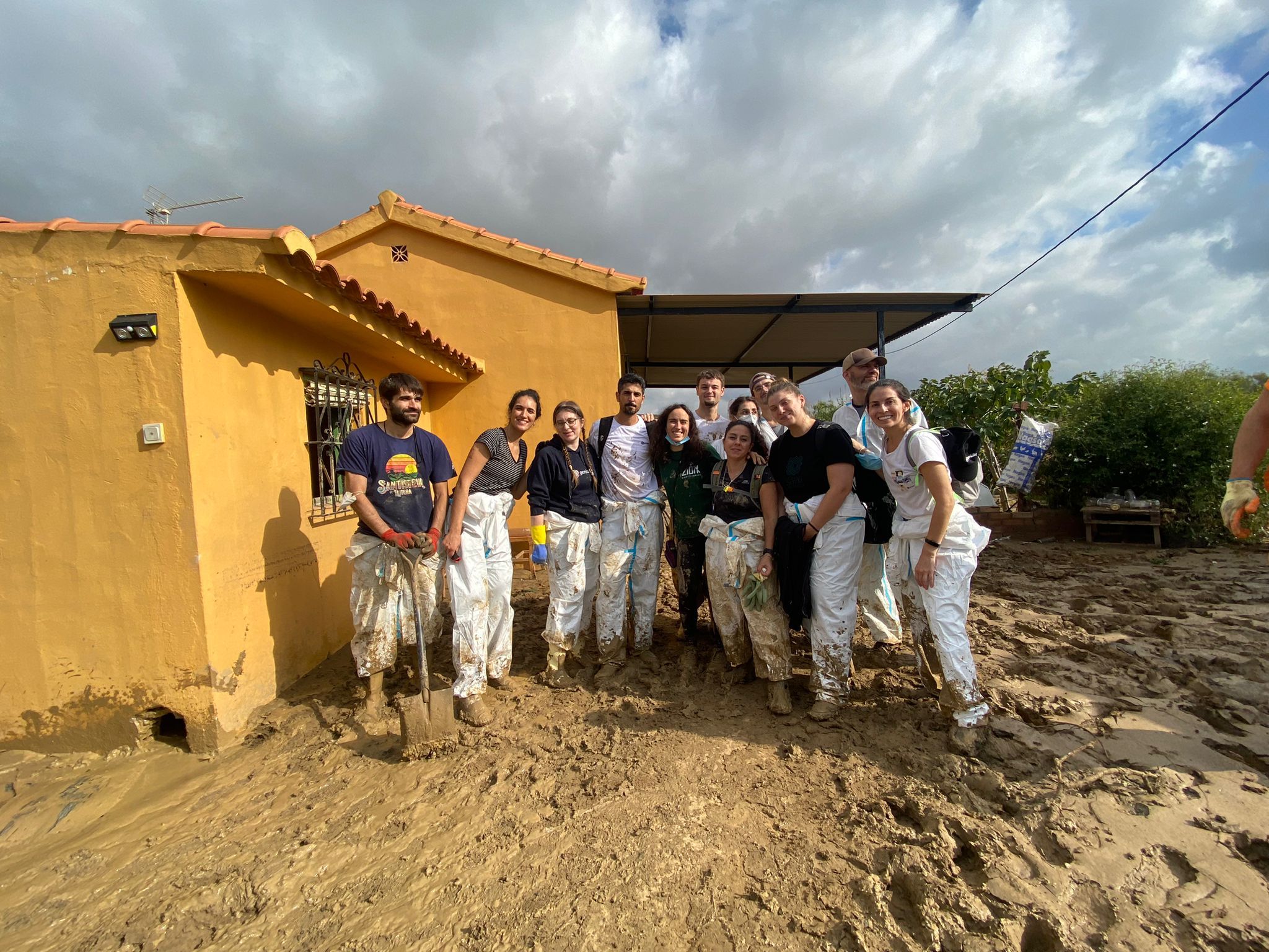 Foto donde aparecemos 12 personas posando de pie, sucios y con barro en el suelo tras haber estado limpiando una casa en las afueras de Álora, Málaga, tras la DANA 2025 que también afectó a esa zona